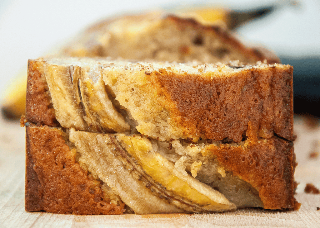 Two slices of Pounamu Protein banana bread on its side with a banana baked on to the top.